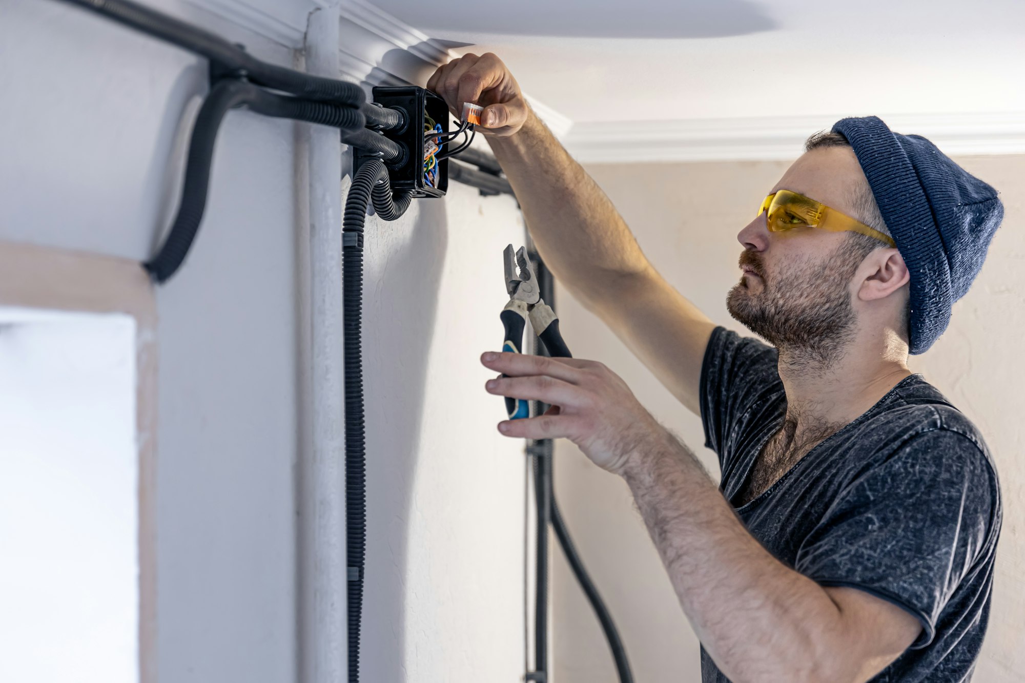 An electrician is mounting electric sockets on the white wall indoors.