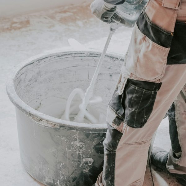 A young caucasian guy a plasterer holds a construction electric mixer and stirs dry putty with water